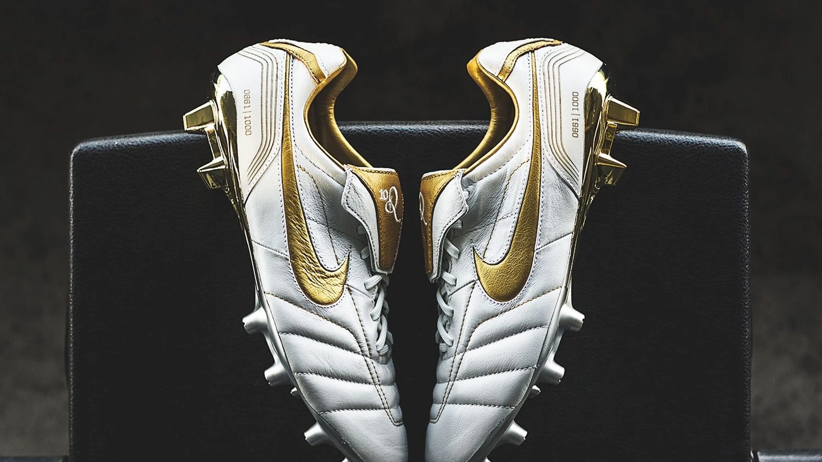 Paire de chaussures de football Nike Tiempo Legend blanche et dorée, posée sur un siège noir