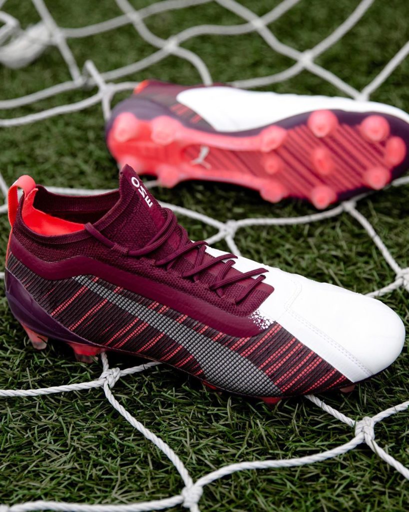 Chaussure de football Puma One bordeaux et blanche posée sur un filet