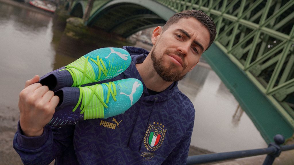 Jorginho tenant une paire de chaussures de football Puma Future Z turquoise
