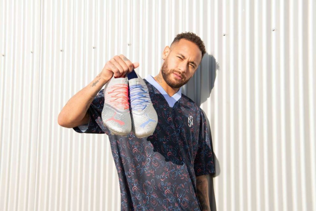 Joueur tenant une paire de chaussures de football Puma Future argentées à reflets irisés