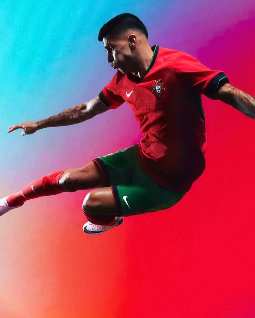 Joueur en maillot rouge et short vert du Portugal en pleine frappe acrobatique, sur fond rouge et bleu