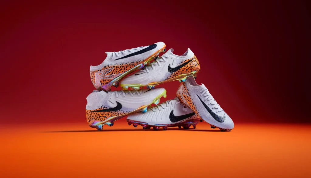Deux chaussures de football Nike blanches aux reflets dorés, posées sur un fond rouge et orange